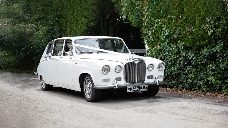White 7-seater Classic Daimler Limousine decorated with ribbons entering wedding venue