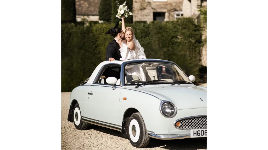 Newly married couple standing inside a Nissan Figaro
