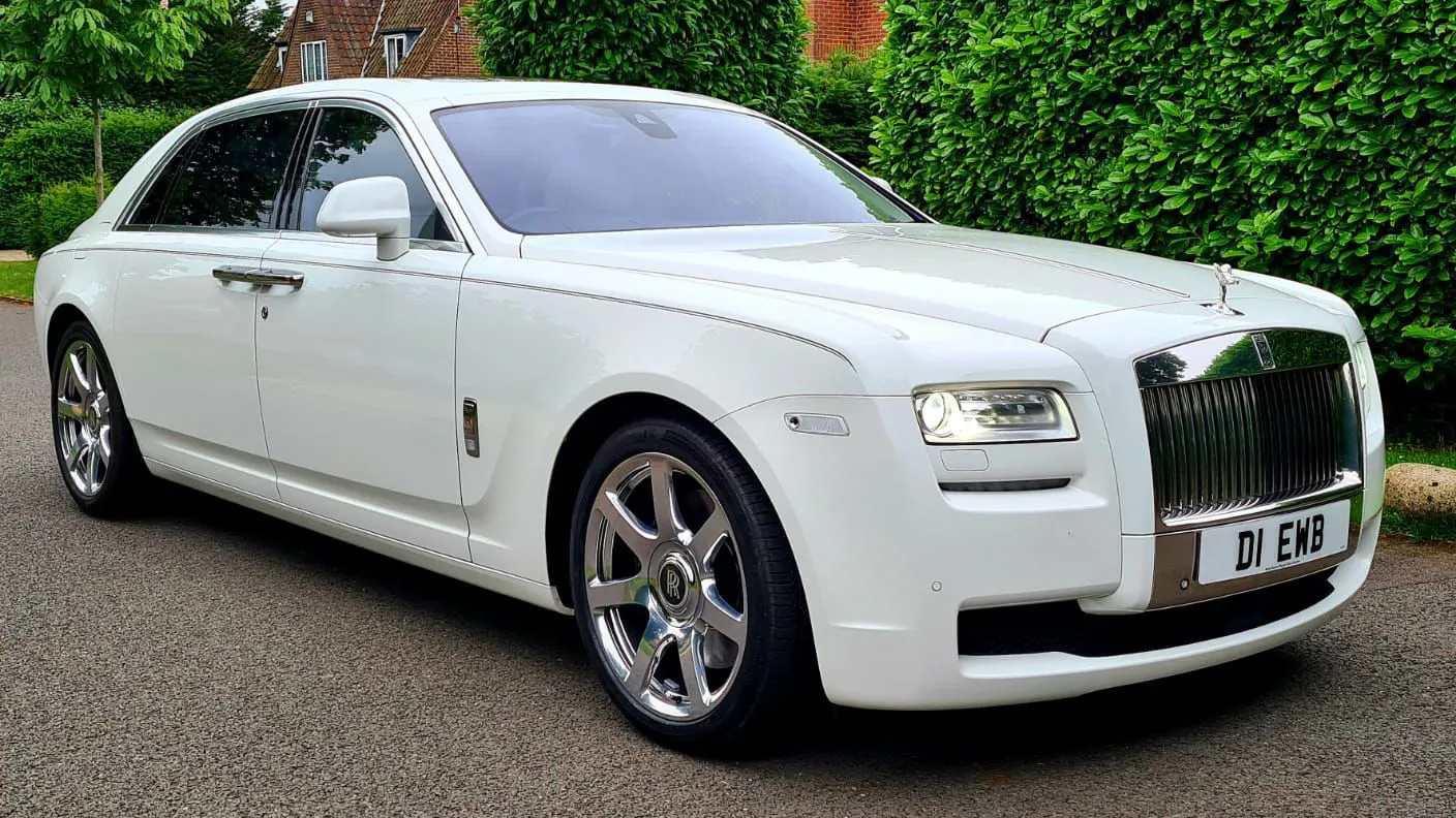 White Rolls-Royce Ghost with chrome front grill and greenery in the background
