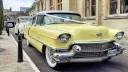 Classic Yellow cadillac decorated with white ribbons parked in front of a cathedral  followed by a second classic car