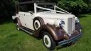 Convertible Vintage Regent in Bronze and Ivory decorated with White ribbons in a green field. Brown Soft Top roof is closed