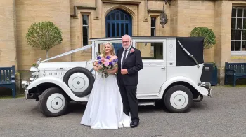 White Imperial Convertible parked in front of wedding venue with Bride and Groom posing for photos in front of the vehicle.