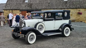 Badsworth Landaulette in Black and ivory dressed with ribbons in front of wedding venue in Newcastle. Wedding Guests can be seen in the background