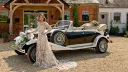 Bride wearing a designer wedding dress posing in front of vintage beauford with convertible roof down