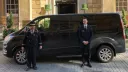 Black Ford Mini Bus in front of hotel with Hotel Doorman and Toastmaster