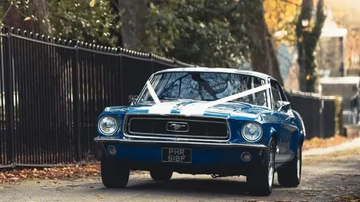 Classic Blue Ford Mustang driving in the street of Bradford with White Ribbons