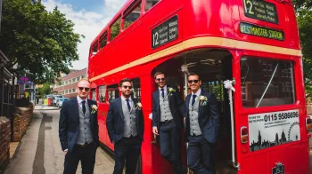 Groom and his three groomsmen standing on the rear open platform of a Classic Double Decker Red Bus