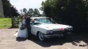 Bride and Groom standing by a Classic Cadilalc decorated with white and pink wedding ribbons