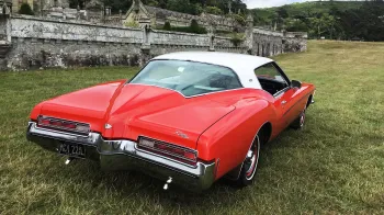 Rear view of classic american Buick from the 70s with red boot and white roof and large rear chrome bumper.