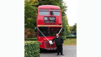 Bus Conductor standing in front of a red Routemaster Bus decorated with white ribbons