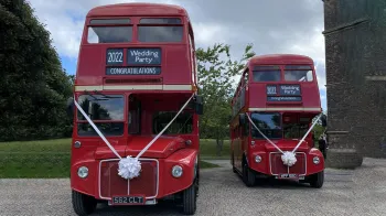 Two identical vintage routemaster buses parked in front of a church in Northumberland