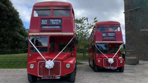 Two identical vintage routemaster buses parked in front of a church in Northumberland