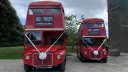 Two identical vintage routemaster buses parked in front of a church in Northumberland
