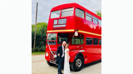 Bride and Groom standing on front of a vintage Red Routemaster Wedding bus decorated with white wedding ribbons