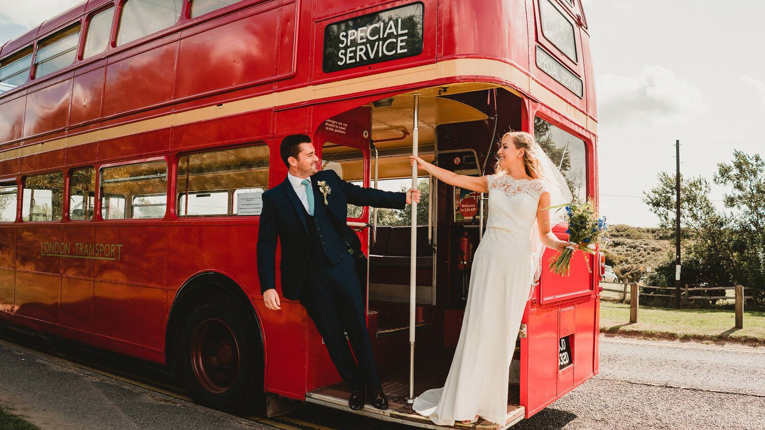 Bride and Groom standing on the rear open platform of an old red routemaster bus