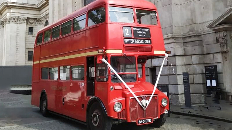 old vintage london red bus parked in the street of London decorated with white wedding ribbons