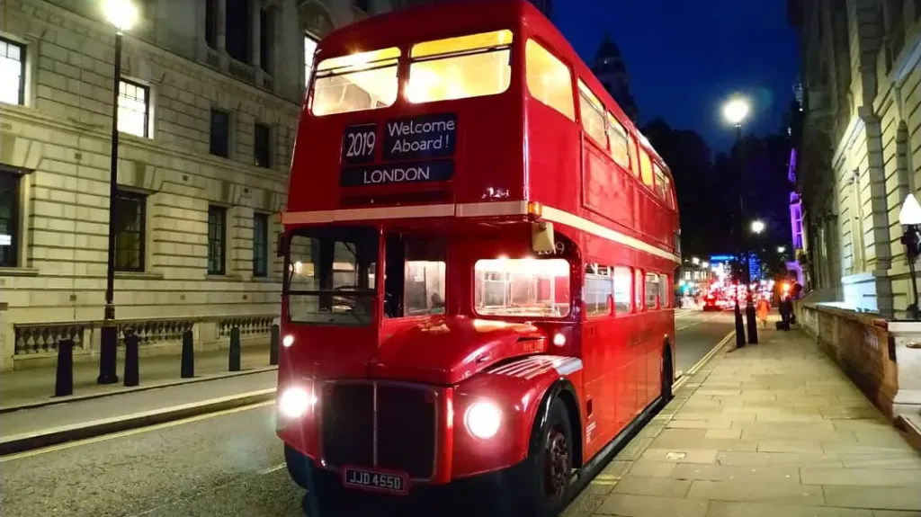 Big Red Double Decker London Routemaster Bus at dusk with lights on