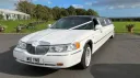 White Stretched Lincoln Limousine with black Roof decorated with pale pink wedding ribbons parked at a wedding venue