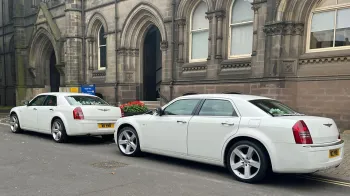 Rear view of two matching Chrysler 300c saloon cars in front of a wedding church in Durham