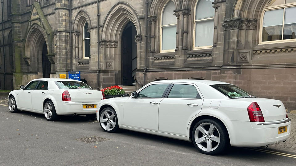 Rear view of two matching Chrysler 300c saloon cars in front of a wedding church in Durham