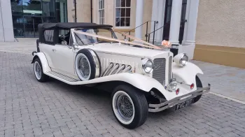 1930s vintage style Beauford convertible in cream with black soft top roof and white wall tires.