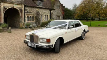 white classic Rolls-Royce Silver Spirit with weding ribbons in front of a wedding venue in Essex
