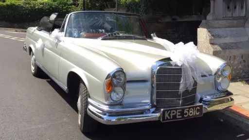 Classic Silver Mercedes se220 with soft top convertible roof down and decorated with white ribbons and large white bows