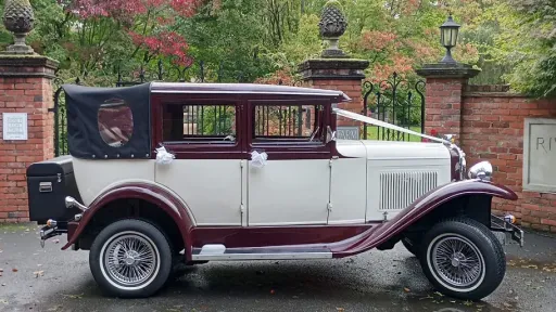 vintage Badsworth wedding car in Ivory with Burgundy wheel arches and roof wth black soft top roof close decorated with ivory ribbons and bows on door handles and rear black picnic trunk