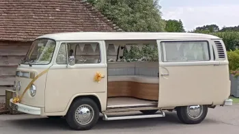 Left side view of a classic VW Campervan with rear door open and decorated with gold ribbons and bows