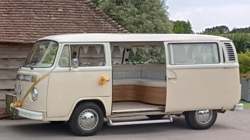Left side view of a classic VW Campervan with rear door open and decorated with gold ribbons and bows