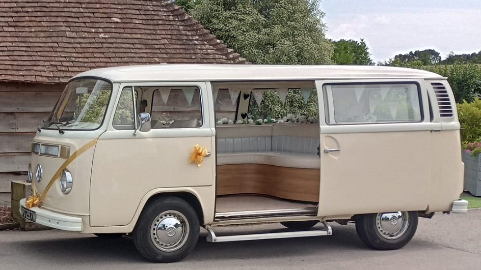 Left side view of a classic VW Campervan with rear door open and decorated with gold ribbons and bows