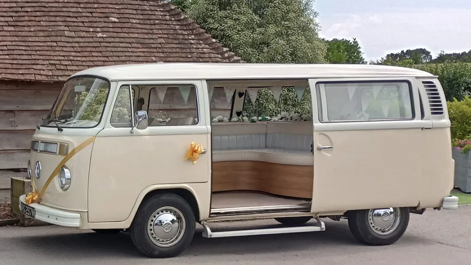 Left side view of a classic VW Campervan with rear door open and decorated with gold ribbons and bows