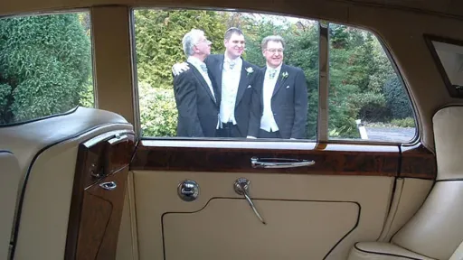 Photo taken frominside a classic Bentley looking at Groom and his two groomsmen through the window