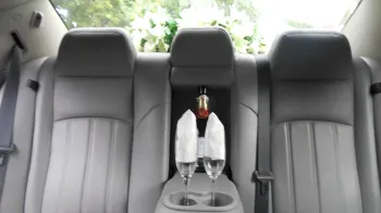 Rear seats inside a chrysler 300c car with a bottle of champagne and two glasses on the centre armrest.