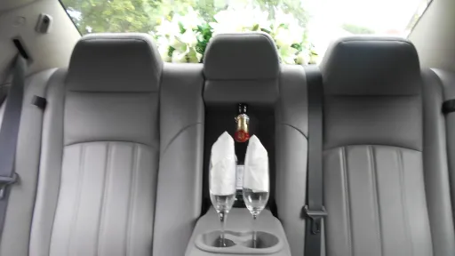 Rear seats inside a chrysler 300c car with a bottle of champagne and two glasses on the centre armrest.