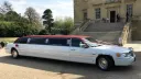 Right side view of white stretched limousine with burgundy roof parked in front of a wedding venue