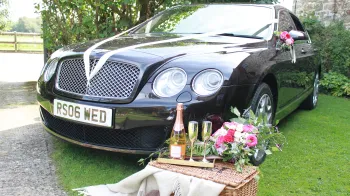 Black Bentley Flying Spur with Champagne bottle and glass on a hamper in front of the vehicle