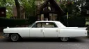 Left side view of a classic White American Cadillac Fleetwood parked in front of a church with Bride walking in the church in the far background