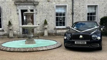 Dark Blue Bentley parked outside wedding venue with white ribbons and bows