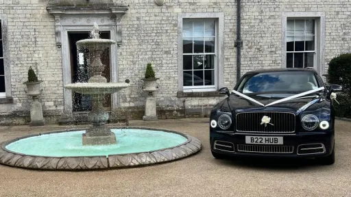Dark Blue Bentley parked outside wedding venue with white ribbons and bows