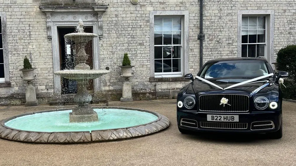 Dark Blue Bentley parked outside wedding venue with white ribbons and bows