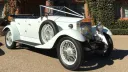 Fully-convertible white vintage Rolls-Royce decorated with white ribbons parked in front of wedding venue in Cheshire