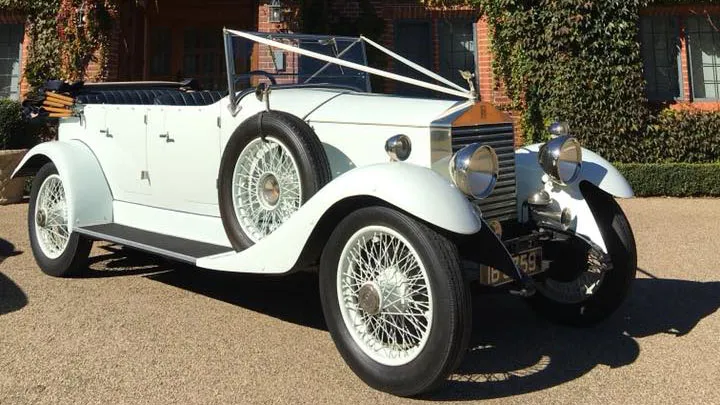 Fully-convertible white vintage Rolls-Royce decorated with white ribbons parked in front of wedding venue in Cheshire