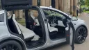 Right side view os a silver tesla X with all doors open showing a cream interior