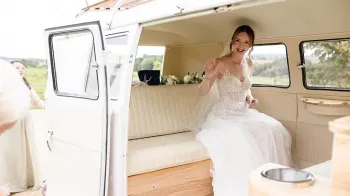 Bride wearing a white wedding dress seating inside a Volkswagen campervan with cream leather interior