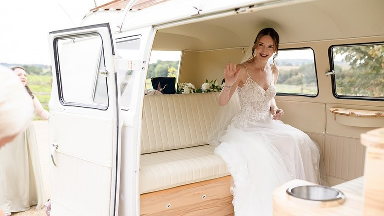 Bride wearing a white wedding dress seating inside a Volkswagen campervan with cream leather interior