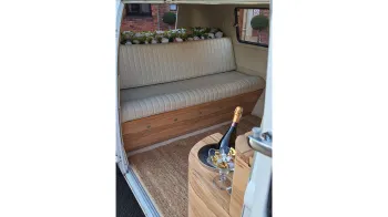 VW Campervan interior with cream leather rear bench seat and a bottle of champagne in a custom built champagne holder.