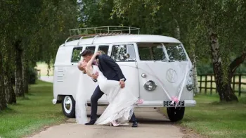 Groom kissing his bride in front of a classic VW Campervan