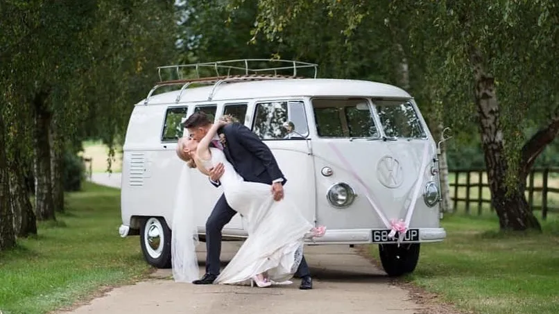 Groom kissing his bride in front of a classic VW Campervan