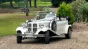 Vintage Beauford Wedding car entering wedding venue with white ribbons across its bonnet